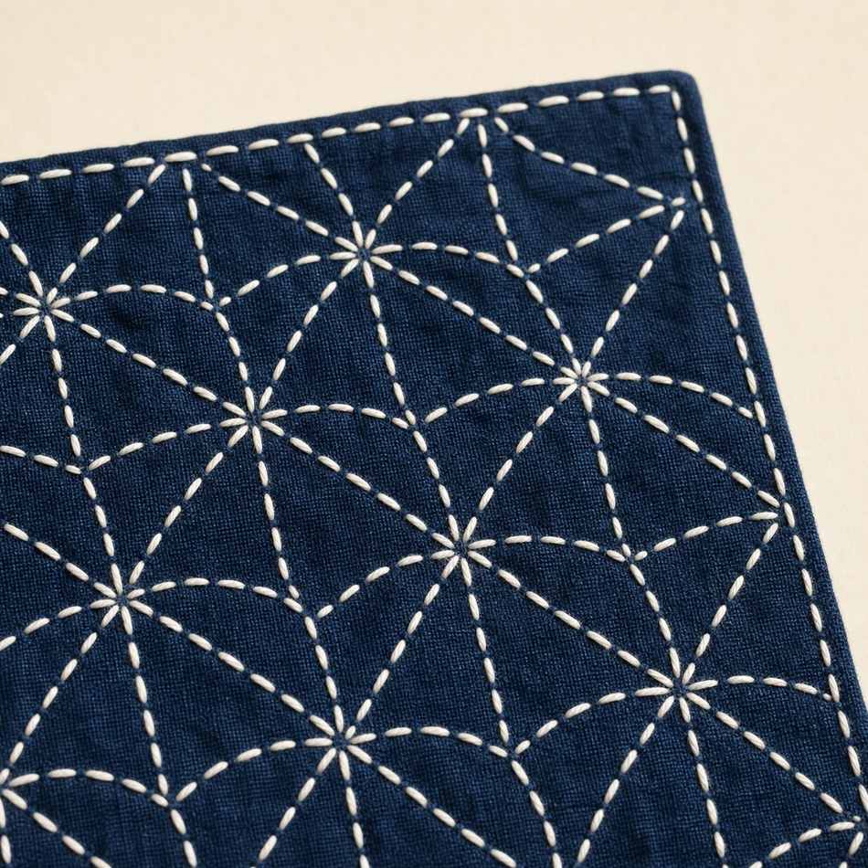 Tissu indigo avec motif sashiko en fil blanc, points réguliers formant un motif géométrique