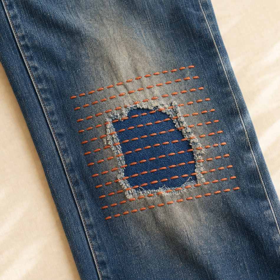 Genou de jean réparé en visible mending avec patch et surpiqûres sashiko en fil terracotta