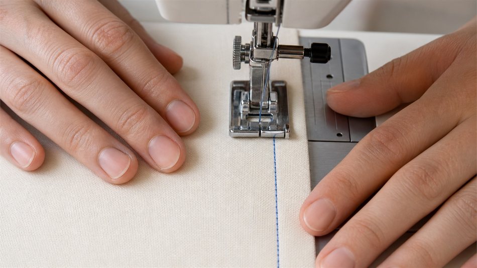 Vue rapprochée de mains posées à plat sur un tissu en cours de couture machine